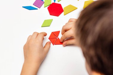 Parlak ahşap tangram oyuncağı oynayan çocuk elleri yakın plan. Çocuk ahşap parmaklık desenleri topluyor. Yaratıcı bebek yeni formlar yapar.