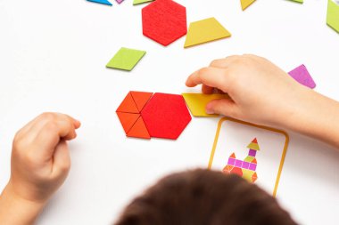 Parlak ahşap tangram oyuncağı oynayan çocuk elleri yakın plan. Çocuk ahşap parmaklık desenleri topluyor. Yaratıcı bebek yeni formlar yapar.
