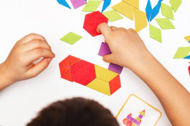 Parlak ahşap tangram oyuncağı oynayan çocuk elleri yakın plan. Çocuk ahşap parmaklık desenleri topluyor. Yaratıcı bebek yeni formlar yapar.