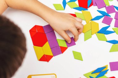 Parlak ahşap tangram oyuncağı oynayan çocuk elleri yakın plan. Çocuk ahşap parmaklık desenleri topluyor. Yaratıcı bebek yeni formlar yapar.