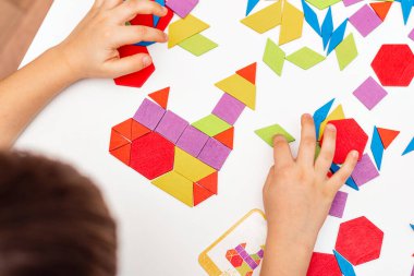Parlak ahşap tangram oyuncağı oynayan çocuk elleri yakın plan. Çocuk ahşap parmaklık desenleri topluyor. Yaratıcı bebek yeni formlar yapar.