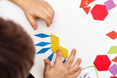 Parlak ahşap tangram oyuncağı oynayan çocuk elleri yakın plan. Çocuk ahşap parmaklık desenleri topluyor. Yaratıcı bebek yeni formlar yapar.