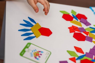 Parlak ahşap tangram oyuncağı oynayan çocuk elleri yakın plan. Çocuk ahşap parmaklık desenleri topluyor. Yaratıcı bebek yeni formlar yapar.