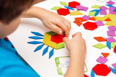 Parlak ahşap tangram oyuncağı oynayan çocuk elleri yakın plan. Çocuk ahşap parmaklık desenleri topluyor. Yaratıcı bebek yeni formlar yapar.