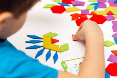 Parlak ahşap tangram oyuncağı oynayan çocuk elleri yakın plan. Çocuk ahşap parmaklık desenleri topluyor. Yaratıcı bebek yeni formlar yapar.