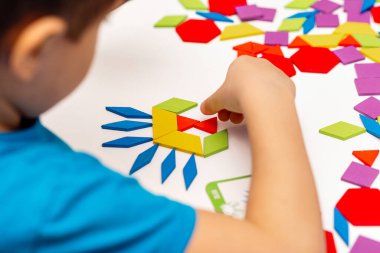 Parlak ahşap tangram oyuncağı oynayan çocuk elleri yakın plan. Çocuk ahşap parmaklık desenleri topluyor. Yaratıcı bebek yeni formlar yapar.