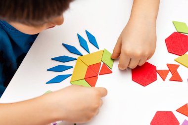 Parlak ahşap tangram oyuncağı oynayan çocuk elleri yakın plan. Çocuk ahşap parmaklık desenleri topluyor. Yaratıcı bebek yeni formlar yapar.
