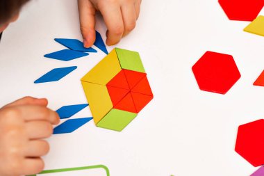 Parlak ahşap tangram oyuncağı oynayan çocuk elleri yakın plan. Çocuk ahşap parmaklık desenleri topluyor. Yaratıcı bebek yeni formlar yapar.