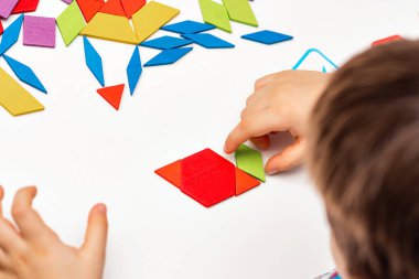 Parlak ahşap tangram oyuncağı oynayan çocuk elleri yakın plan. Çocuk ahşap parmaklık desenleri topluyor. Yaratıcı bebek yeni formlar yapar.