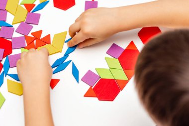 Parlak ahşap tangram oyuncağı oynayan çocuk elleri yakın plan. Çocuk ahşap parmaklık desenleri topluyor. Yaratıcı bebek yeni formlar yapar.