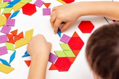 Parlak ahşap tangram oyuncağı oynayan çocuk elleri yakın plan. Çocuk ahşap parmaklık desenleri topluyor. Yaratıcı bebek yeni formlar yapar.