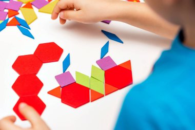 Parlak ahşap tangram oyuncağı oynayan çocuk elleri yakın plan. Çocuk ahşap parmaklık desenleri topluyor. Yaratıcı bebek yeni formlar yapar.