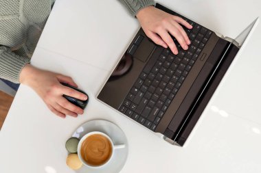 Bilgisayarın başında bir fincan kahveyle çalışan bir kadının elleri. Uzaktan çalışma, ev ofisi, serbest çalışma, online öğrenme