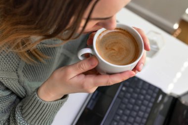 Kahve içen ve dijital tablet kullanan bir kadın, dizüstü bilgisayar. Masada oturuyor.