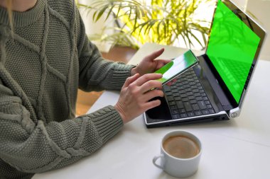 Bir kadın dizüstü bilgisayarda çalışıyor ve telefonunun ekranına bakıyor. Çevrimiçi alışveriş, serbest çalışma, öğrenme, iletişim kavramı