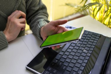 Bir kadın dizüstü bilgisayarda çalışıyor ve telefonunun ekranına bakıyor. Çevrimiçi alışveriş, serbest çalışma, öğrenme, iletişim kavramı