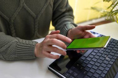 Bir kadın dizüstü bilgisayarda çalışıyor ve telefonunun ekranına bakıyor. Çevrimiçi alışveriş, serbest çalışma, öğrenme, iletişim kavramı