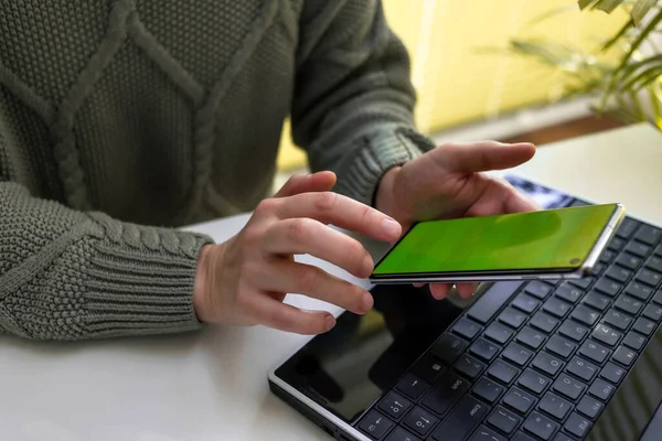 Bir kadın dizüstü bilgisayarda çalışıyor ve telefonunun ekranına bakıyor. Çevrimiçi alışveriş, serbest çalışma, öğrenme, iletişim kavramı