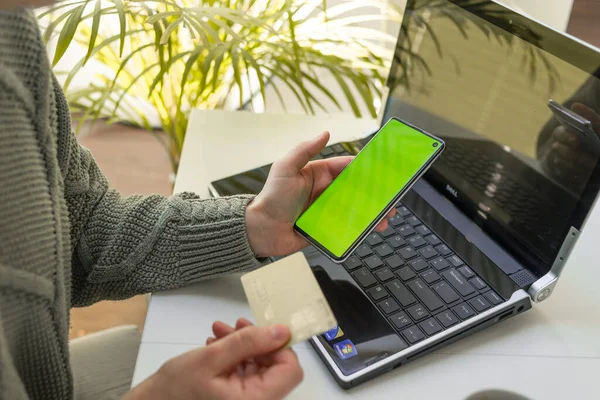 Stock image A woman works on a laptop and looks at the screen of her phone. The concept of online shopping, freelancing, learning, communication