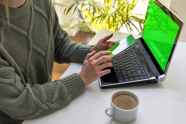 stock image A woman works on a laptop and looks at the screen of her phone. The concept of online shopping, freelancing, learning, communication