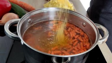 Çorba yapma süreci. Ev mutfağında yemek pişirmek için gerekli malzemeler bir tencereye konur. Kadının elleri kapalı.
