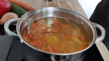 Çorba yapma süreci. Ev mutfağında yemek pişirmek için gerekli malzemeler bir tencereye konur. Kadının elleri kapalı.