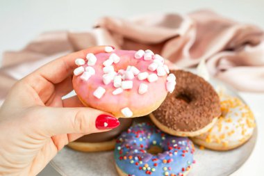 Renkli arkaplanda lezzetli donutlar olan el, tabaktan bir donut alır.