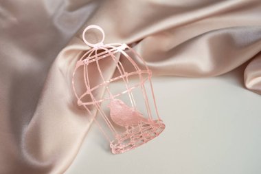 Üzerinde pembe ipek kumaştan yapılmış arka planda bir kuş olan pembe kağıt kafes. Yazı için arka plan fotoğrafı. Tebrik ederim.
