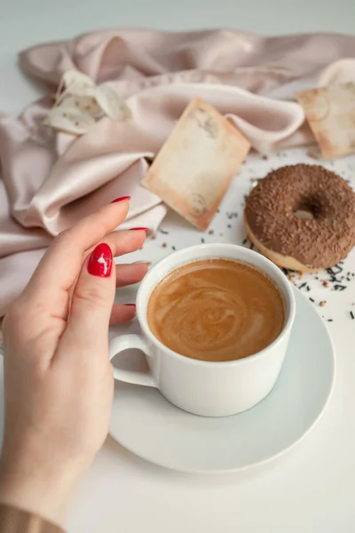 stock image Close-up of a cup of coffee held by a woman's hand. On the background are paper cards and delicate silk drapery