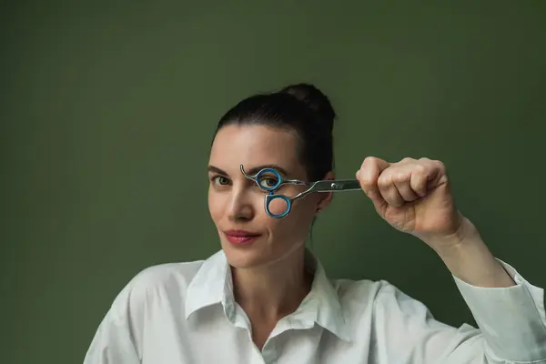 stock image Photo of a hairdresser, a master, with professional scissors in her hands, wearing a white shirt against an isolated green background