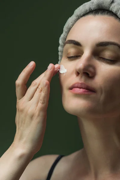 An attractive European woman puts cream on her face. Close-up of the beauty industry, cosmetology. Skin care at home