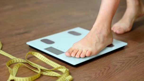 白色的地板鳞片和站在上面的女人的脚 测量身体变化的裁缝厘米或测量带 健康生活方式和体重跟踪的概念 — 图库视频影像