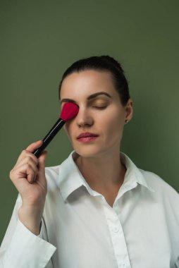 Makyöz pudrası ve fırçası. Güzel kadın yüzü. Kadın yanaklarına allık sürüyor. Telafi sürecinde. Avrupalı kadın makyaj fırçası kullanıyor