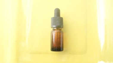 Sarı cam bir yüzey üzerinde pipetli kahverengi cam kozmetik şişesi bulunur. Şişedeki su spreyinin en üst görüntüsü. Tasarım ve reklam için örnek paketleme
