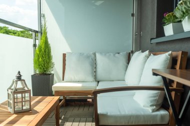 Şirin modern balkon ahşap kanepe selvi ve çiçeklerle süslenmiş masa ve masanın üzerinde dekoratif bir fener.