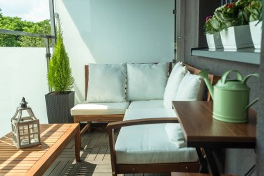 Şirin modern balkon ahşap kanepe selvi ve çiçeklerle süslenmiş masa ve masanın üzerinde dekoratif bir fener.