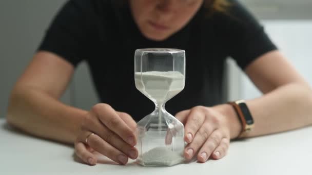 女性はテーブルに座って砂時計を見て それをひっくり返します 時間の逆転 女は時間が尽きていることを強調される — ストック動画