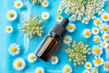 İçinde pipetle birlikte gerekli yağ şişesi ya da şişe mavi arka planda çiçeklerle çevrili olarak suyun içinde yatar. Reklam, güzellik endüstrisi, kozmetoloji, tıp için arka plan