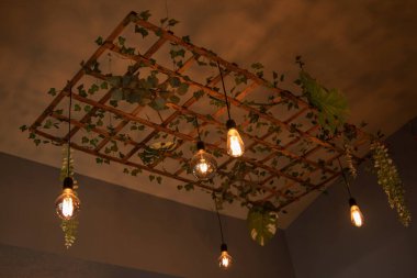 Bitkilerle süslenmiş ahşap örgüden yapılmış modern bir lamba. İç aydınlatmanın modern tasarımı