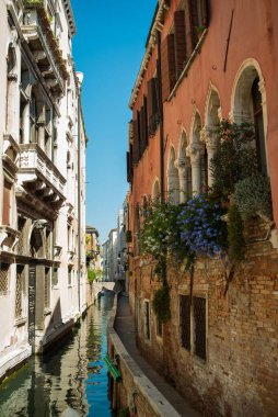 Venedik kanalı manzarası. Tekneleri ve çiçekli eski evleri var. Turistik bir yer, bir yolculuk. Venedik, İtalya, 08.19.2023