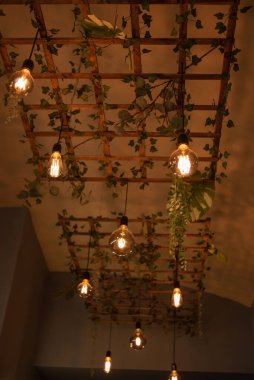 Bitkilerle süslenmiş ahşap örgüden yapılmış modern bir lamba. İç aydınlatmanın modern tasarımı