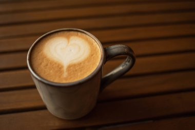 Ahşap bir masada kapuçino bardağı. Kil bardakta kahve. Cappuccino köpüklü bir kalp. Retro tarzı. Kopyalanacak yer