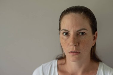 Yargılayıcı bir bakış. Gri arka planda şüphe ve kınamayı resmeden bir kadın portresi. Yakın plan.