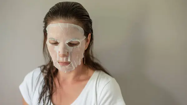 woman with a fabric cosmetic mask on her face, does skin care. Close-up portrait on a gray background. The beauty industry, self-care.