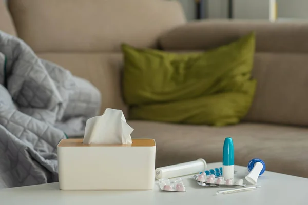 Cold medicine on the background of a sofa with pillows and a blanket. Tablets, spray and thermometer are on the table against the background of a place to relax