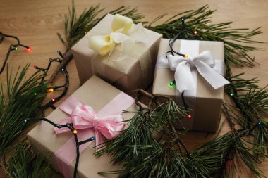 El işi kağıdında sarı kurdele, çam dalları, koniler ve ahşap masada bir çelenk.