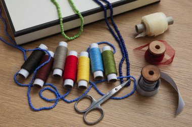 Çok renkli iplikli makaralar ve kurdeleler, makas ve boncuklu iplikler ahşap bir masanın üzerinde yatıyor.