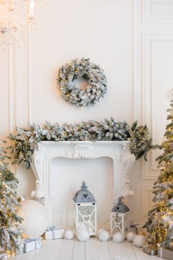 Şömineli beyaz bir oda, yapay kar ve çelenkli Noel ağaçları, bir kanepe, yastıklı bir ekose, fenerli bir beyaz oyuncak ayı, içinde yılbaşı hediyeleri olan kutular, bir çelenk.