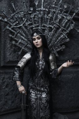 Zırhlı güzel savaşçı prenses bir kılıç tutuyor. Fantezi cadı şövalye siyah saçlı kadın çelenk giyiyor. Peri masalı gotik kraliçesi.