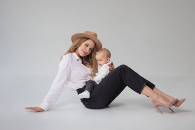 Stüdyoda yerde oturan anne ve çocuğun moda portresi. Kızıyla birlikte genç bir kadın.